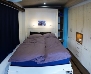 Une chambre à coucher avec un lit, une table de chevet, une étagère avec un tableau, et une armoire.