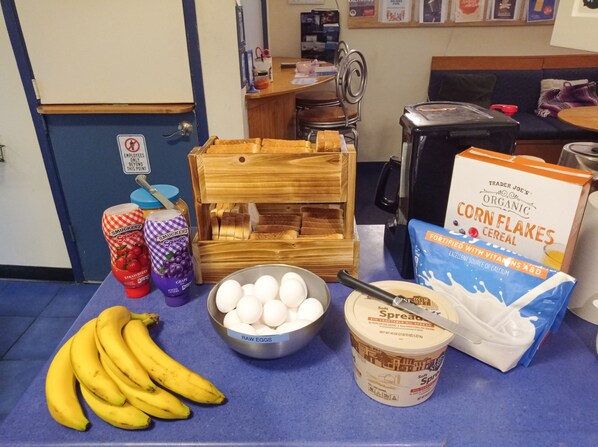 Una mesa con alimentos como plátanos, huevos, mermelada de uva Smucker's y copos de maíz orgánicos de Trader Joe's.