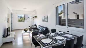 Een moderne eethoek met een zwart-wit gedekte tafel voor vier personen, een zwarte leren bank en een groot raam met uitzicht op de omgeving.