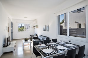 Ein moderner Essbereich mit einem schwarz-weißen Tisch, gedeckt für vier Personen, einer schwarzen Ledersofa und einem großen Fenster mit Blick ins Freie.