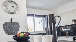 Een moderne keuken met een zwart aanrecht, een roestvrijstalen waterkoker, een schaal met appels en een klok aan de muur.
