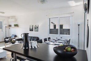 Un coin repas moderne avec une table noire dressée pour quatre personnes, des chaises blanches et un saladier noir contenant des pommes.