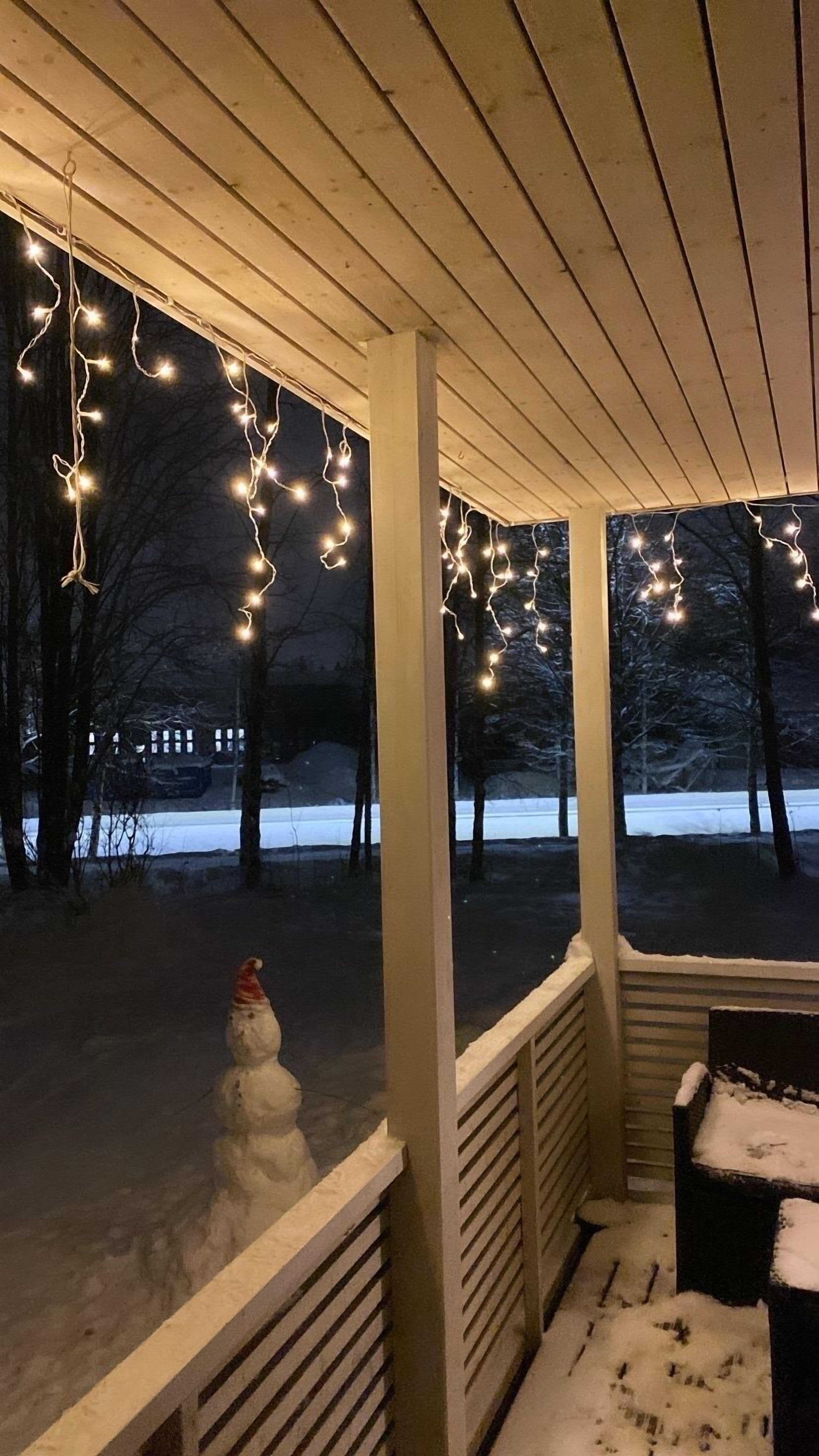 A covered porch with string lights and a snowman.