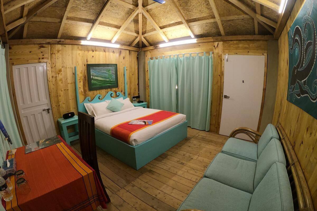 A wooden cabin bedroom with a bed, a small table, a chair, and a door.