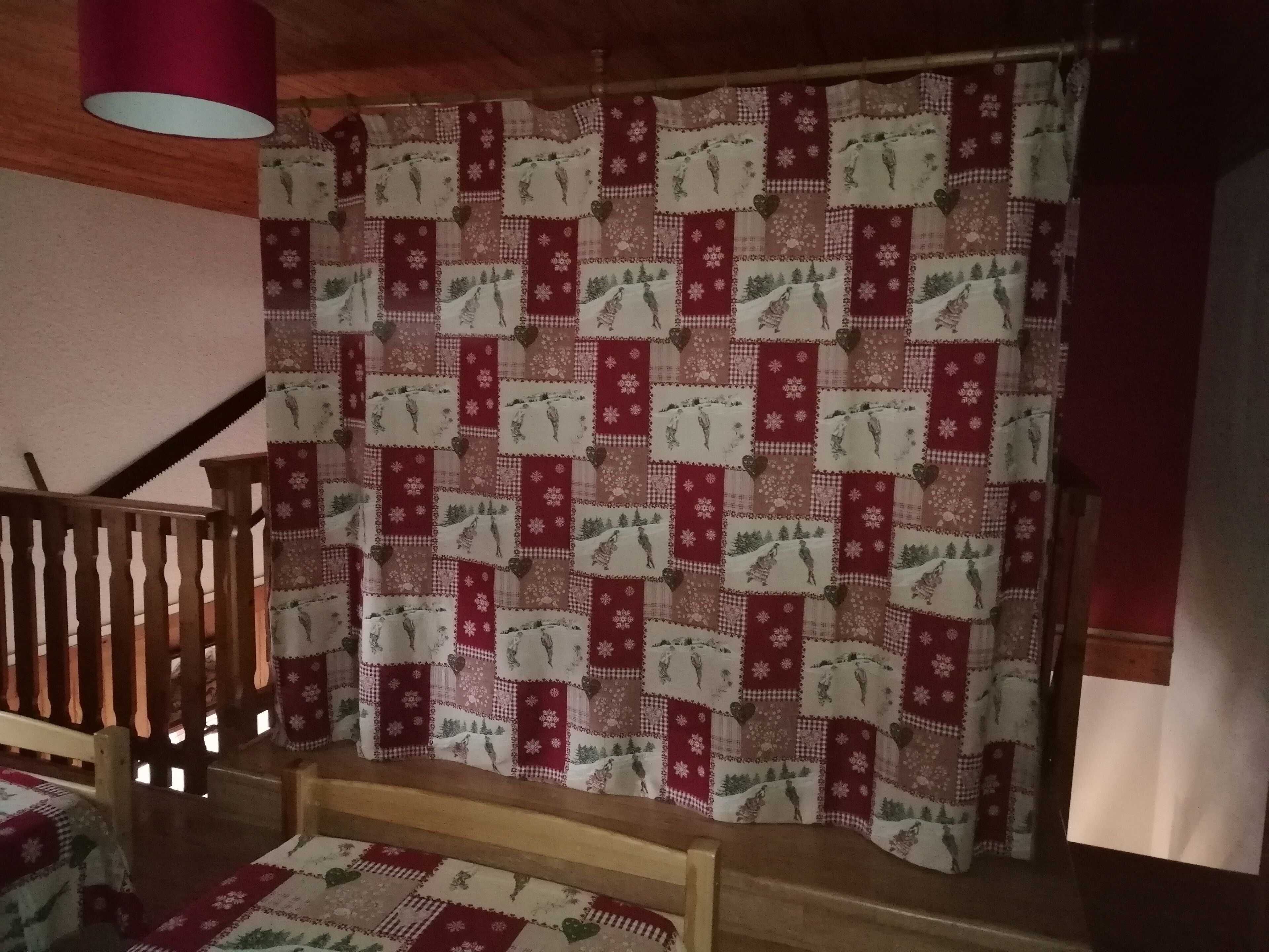 Una habitación con una escalera de madera, una cortina estampada y una cama con colcha.