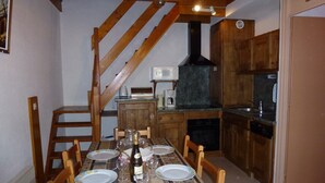 A dining area with a wooden table set for four, surrounded by chairs. A staircase leads to an upper level. The kitchen is visible with wooden cabinets and a stove. - Superb 2 room apartment (1 bedroom) + mezzanine ...... at the foot of the slopes! (Lanslevillard)