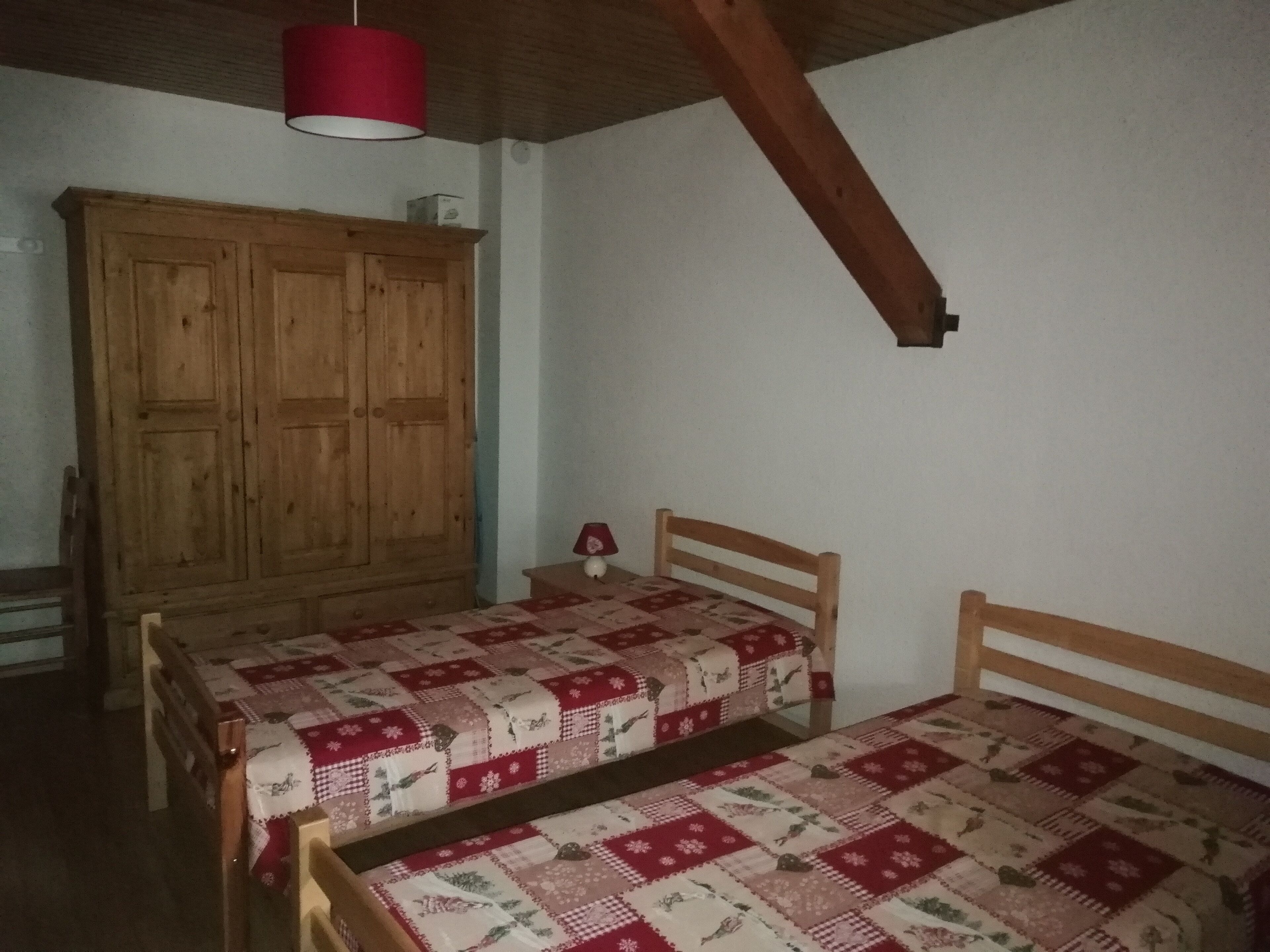 Ein Zimmer mit zwei Holzbetten, einem großen Holzschrank und einer roten Hängeleuchte.