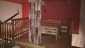 A bedroom with a wooden bed, a nightstand, a lamp, a patterned curtain, and a staircase with a railing. - Superb 2 room apartment (1 bedroom) + mezzanine ...... at the foot of the slopes! (Lanslevillard)