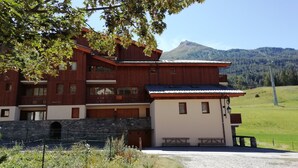 A multi-story wooden building with balconies, a stone foundation, and a view of a mountain. - Superb 2 room apartment (1 bedroom) + mezzanine ...... at the foot of the slopes! (Lanslevillard)