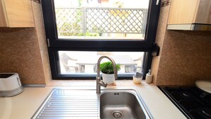 Una cocina con un lavamanos de acero inoxidable, una ventana con vista a muebles de exterior y una estufa.