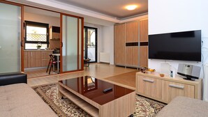 Una sala de estar moderna con un televisor de pantalla plana, muebles de madera, una mesa de centro y un ventanal corredero que da a un balcón.