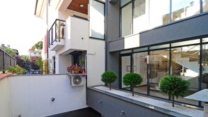 Un edificio moderno con un balcón, un pequeño jardín con plantas en macetas y una ventana con vista a una escalera.