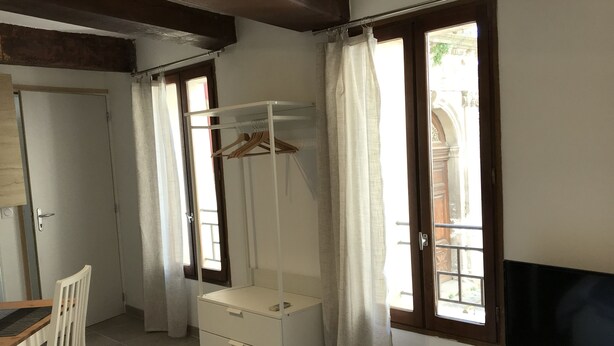 A room with a bed, a desk, a chair, a TV, a wardrobe, and a window with curtains.