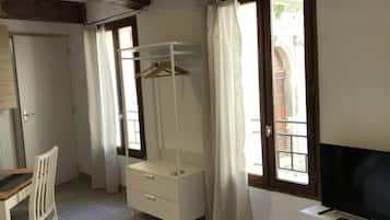 Une chambre comprenant un lit, un bureau, une chaise, une télévision, une armoire et une fenêtre avec des rideaux.
