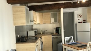 A compact kitchen with wooden cabinets, a built-in dishwasher, a coffee maker, and a refrigerator.
