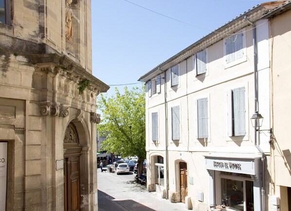 A narrow street with historic buildings, a café, and parked cars.