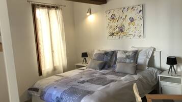 Une chambre à coucher avec un lit, deux tables de chevet, une lampe sur chaque table, une fenêtre avec des rideaux et un tableau floral accroché au mur.