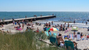 Ein Strand mit einer Seebrücke, Liegestühlen, Sonnenschirmen und Menschen, die das Meer genießen.