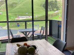 En balkon med et bord og stole, der vender ud mod et græsområde med køer og en mindre bygning.