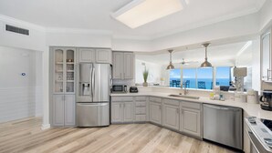 Una cocina moderna con una isla grande, electrodomésticos integrados y vista al océano.