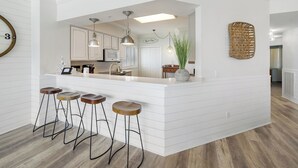 Una cocina moderna con una isla central, taburetes de bar, iluminación colgante y una planta decorativa.