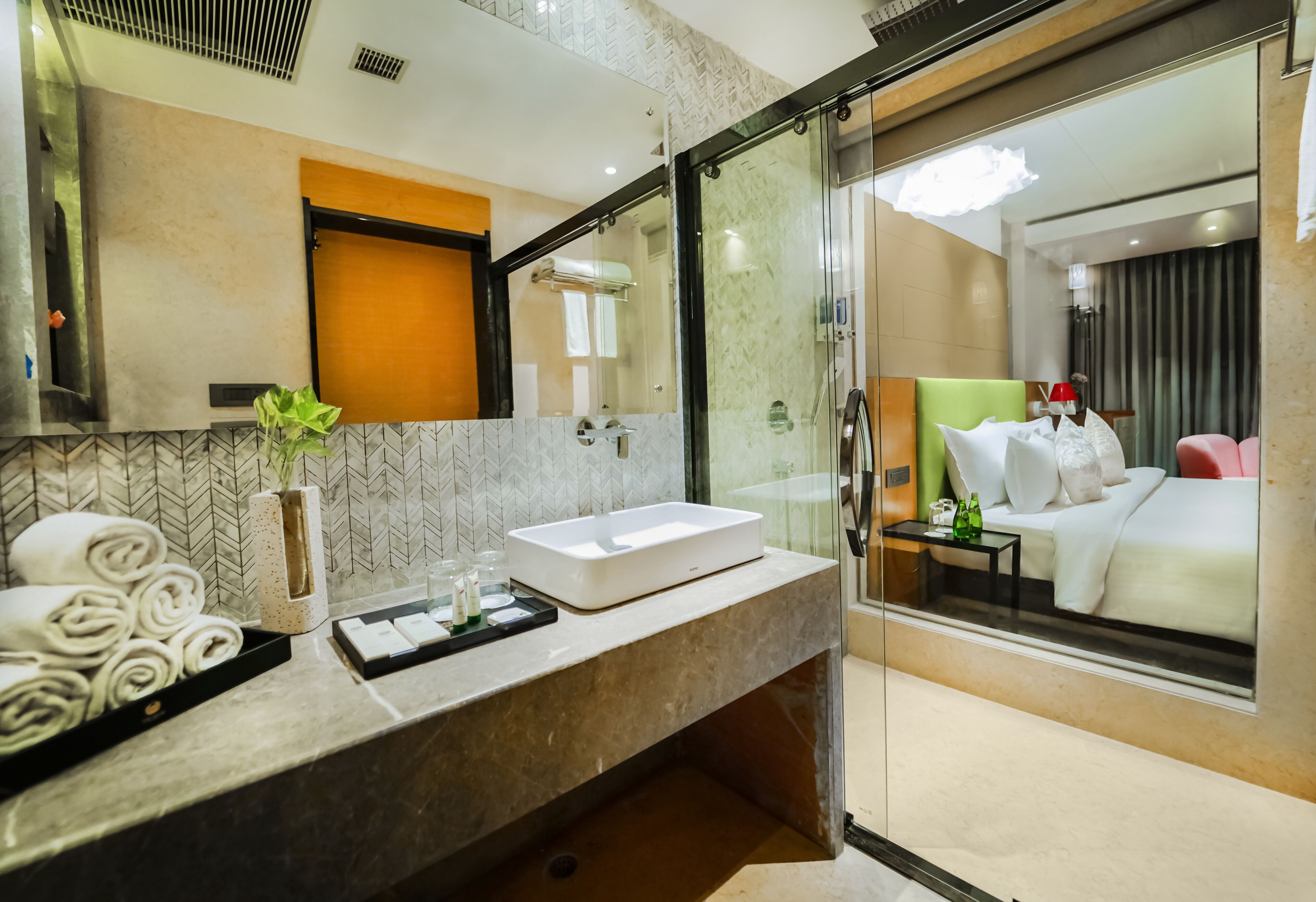 A modern hotel bathroom with a large mirror, a sink, and a glass-enclosed shower.