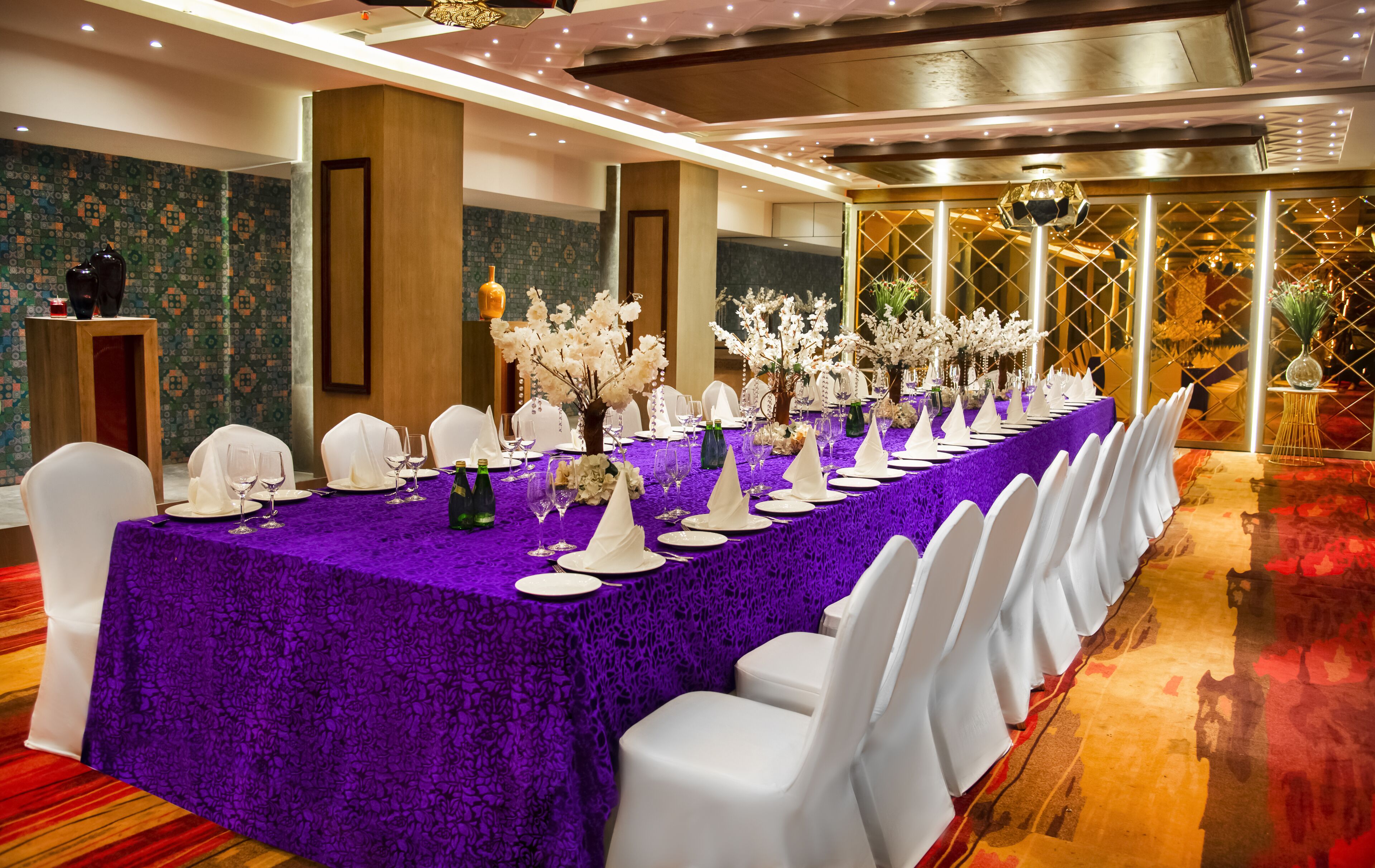 A banquet hall with a long table covered in purple tablecloths, white chairs, and floral centerpieces.