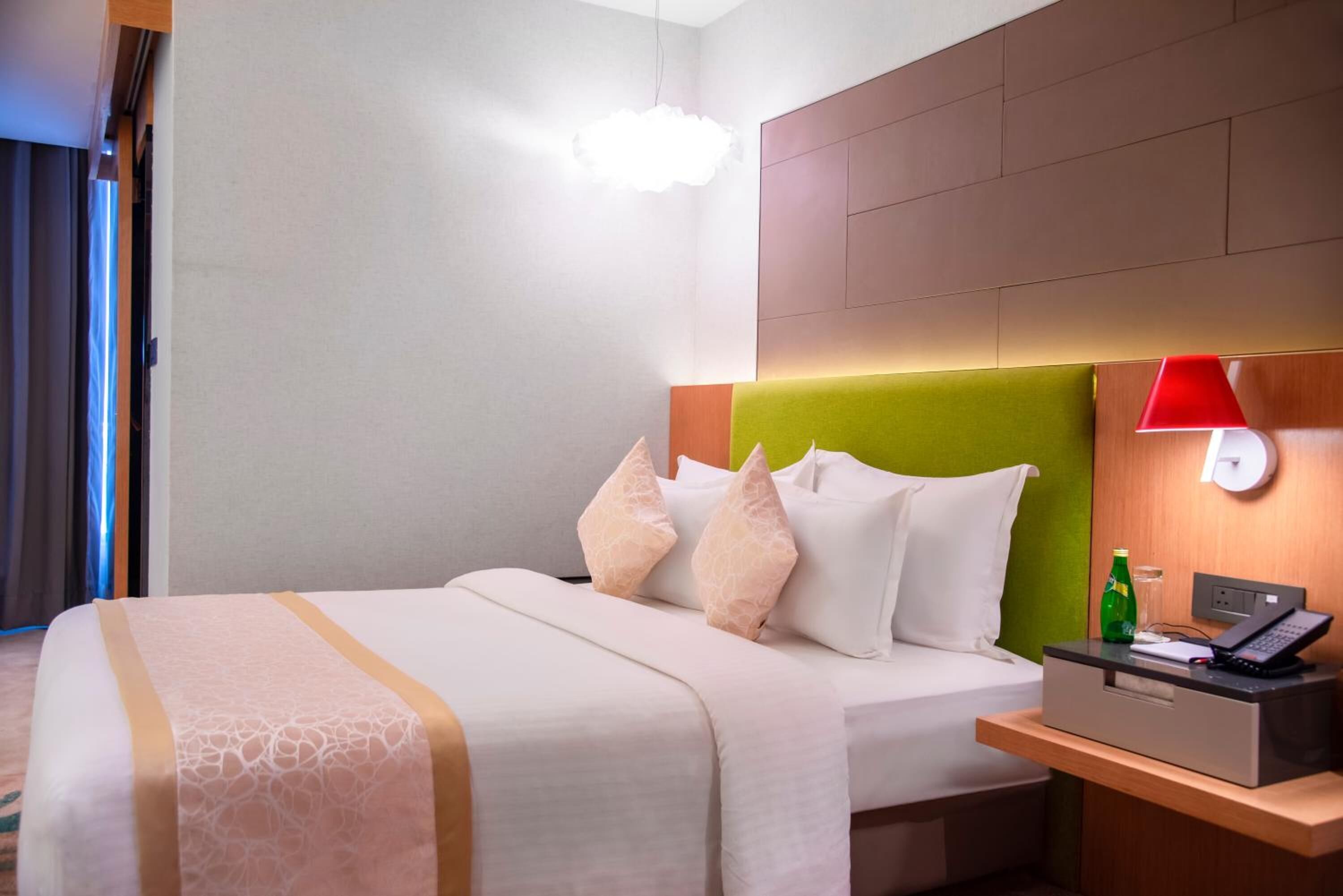 Una habitación de hotel con cama, mesita de noche, lámpara y teléfono en la pared.