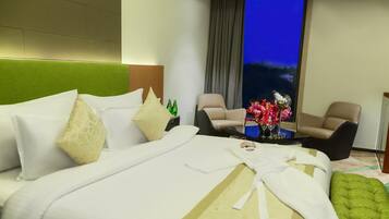 Habitación de hotel con una cama grande, dos sillones, una mesita con un florero y vistas al cielo nocturno.