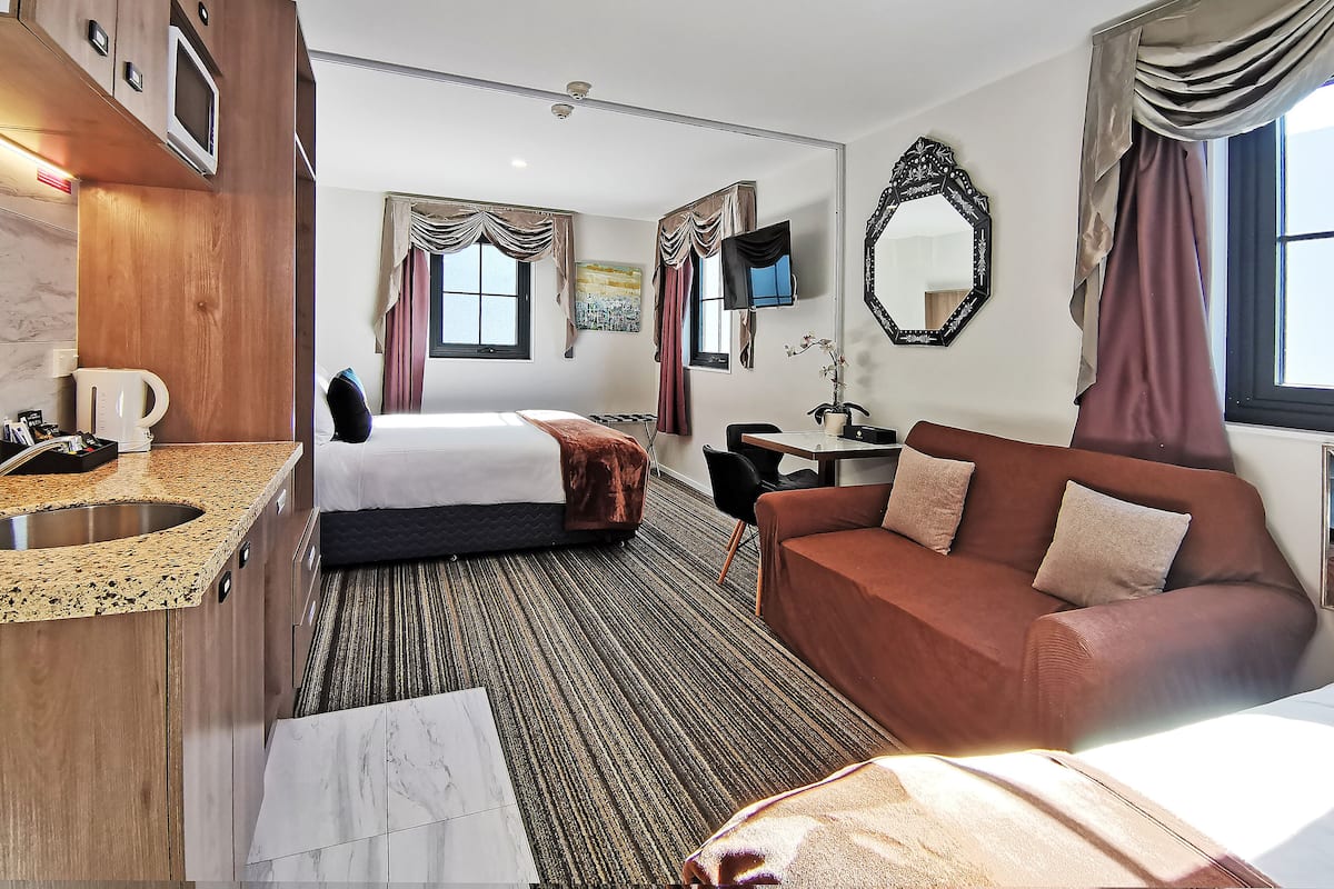 A hotel room with a bed, a sofa, a desk, a TV, a mirror, and a window with curtains.