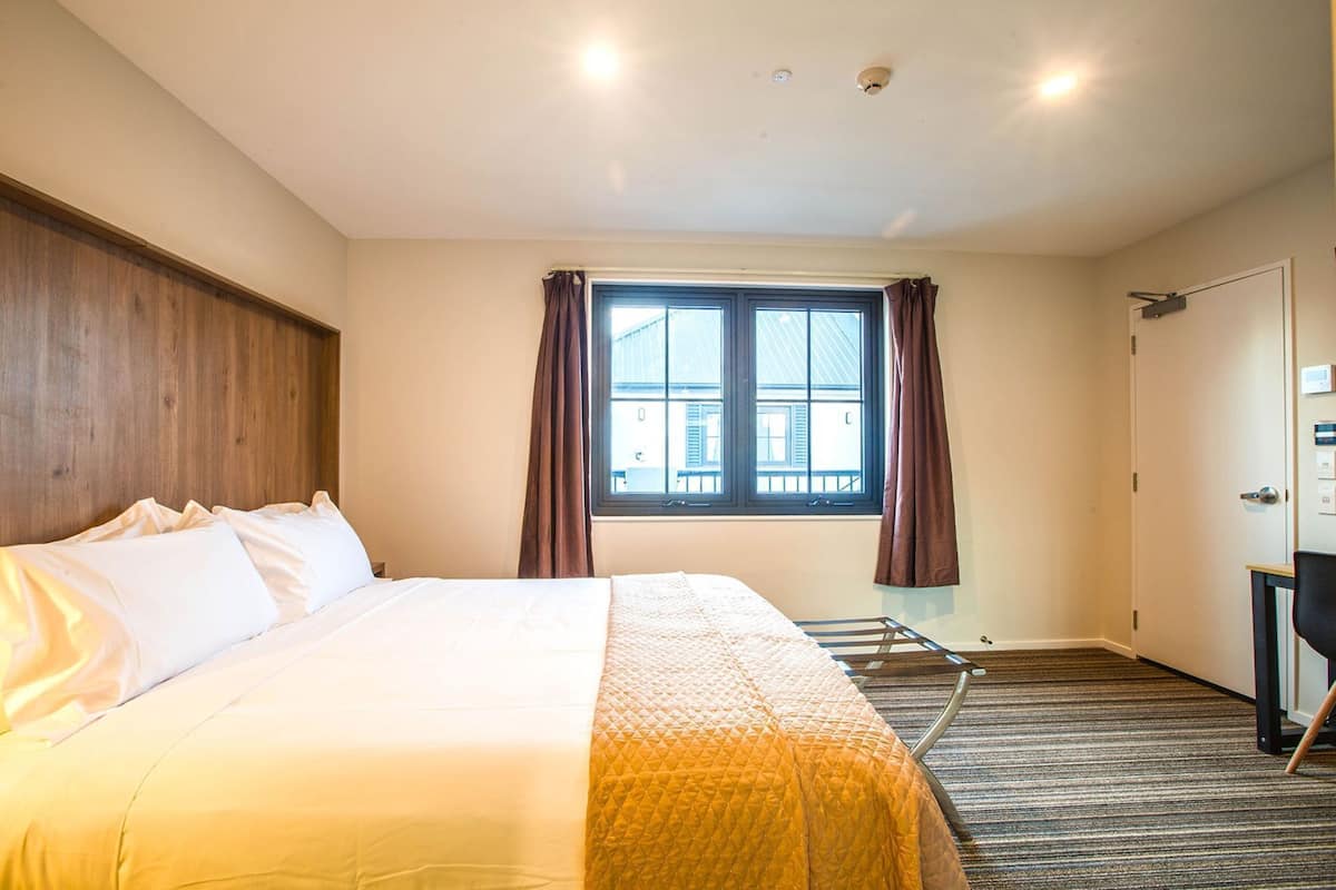 A hotel room with a bed, a window with curtains, a door, and a small table.