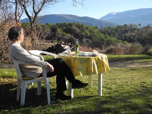 Une personne est assise à une table à l’extérieur, avec une vue sur les montagnes en arrière-plan.