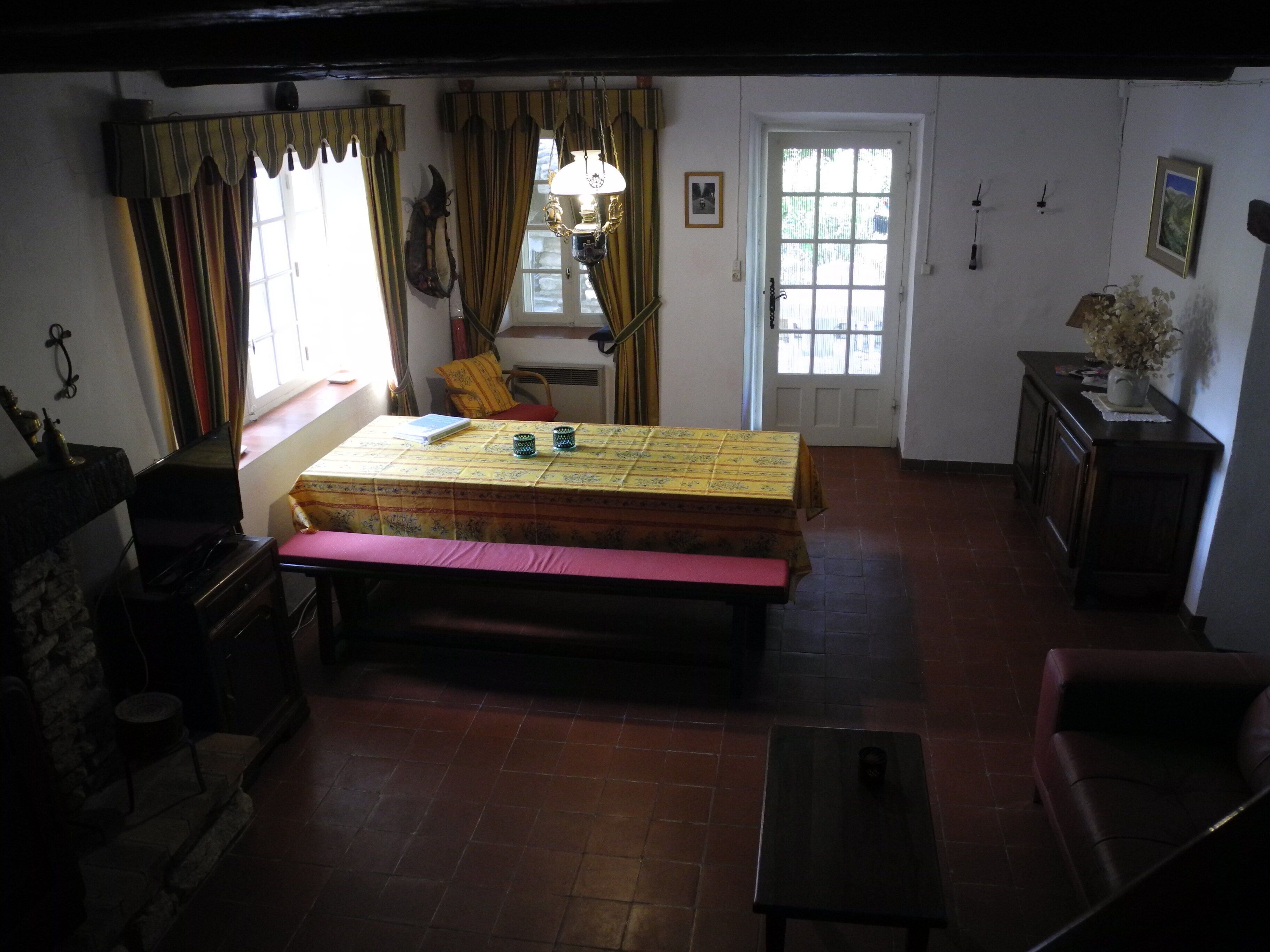 A room with a bed, a table with a yellow tablecloth, a bench, a chair, a small table, a sofa, and a fireplace.