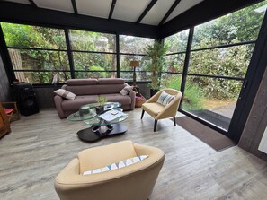 Un intérieur moderne avec un canapé, un fauteuil et une table basse en verre, de grandes fenêtres offrant une vue sur la verdure.