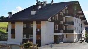 Ein mehrgeschossiges Gebäude mit einem geneigten Dach, großen Fenstern und einem Balkon im oberen Stockwerk.