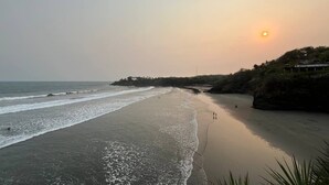 Une plage au coucher du soleil, avec des vagues calmes et quelques personnes se promenant le long du rivage.