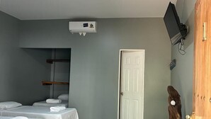 Une chambre d’hôtel avec deux lits, un téléviseur fixé au mur, une armoire en bois et une porte.
