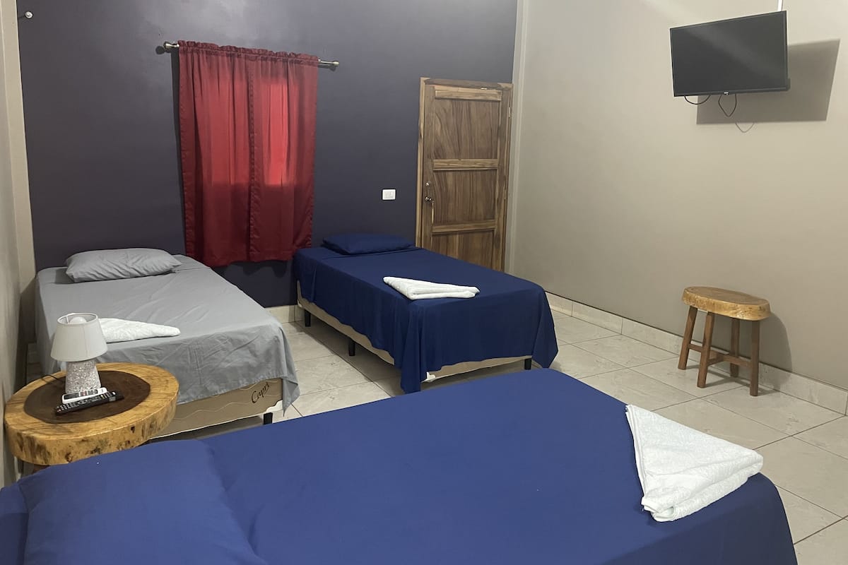 Ein Zimmer mit zwei Einzelbetten, einem an der Wand montierten Fernseher, einer Holztür und einem kleinen Hocker.