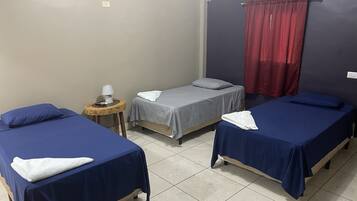 A room with three single beds, a small round table with a lamp, and a red curtain.