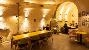 A dining area with a long wooden table and chairs, a small round table with a chair, and a seating area with a sofa and armchairs. - Lemon Cave Suites And Coffee House (Avanos)
