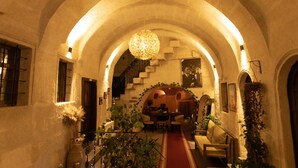 An arched hallway with a dining area at the end, featuring a red carpet, potted plants, and a hanging light fixture. - Lemon Cave Suites And Coffee House (Avanos)