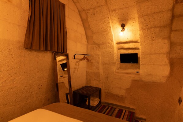 A room with a bed, a small table, a hanging coat rack, a window with a light fixture, and a striped rug.