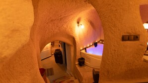 A narrow, tunnel-like passageway leading to a room with a bathtub, a sink, and a mirror with lights. - Lemon Cave Suites And Coffee House (Avanos)