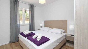A hotel room with a bed, two bedside lamps, a window with curtains, and a nightstand. - Holiday apartment, modernly furnished, only 300 m from the sea (Baška)