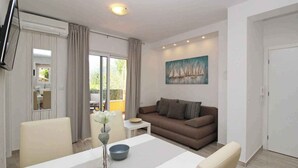 A modern living room with a brown sofa, a dining table with chairs, a flat-screen TV mounted on the wall, and a painting of sailboats. - Holiday apartment, modernly furnished, only 300 m from the sea (Baška)
