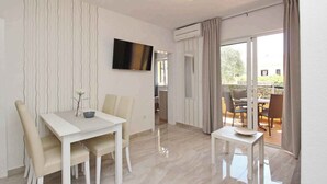 A modern living room with a dining area, a flat-screen TV, and a sliding glass door leading to an outdoor patio. - Holiday apartment, modernly furnished, only 300 m from the sea (Baška)