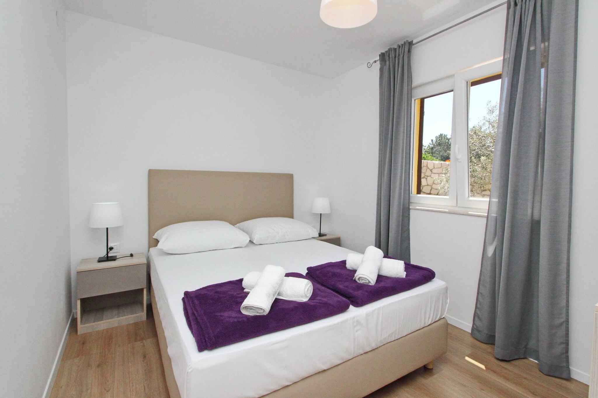 Ein Hotelzimmer mit Bett, zwei Nachttischen, einem Fenster mit Vorhängen und Blick nach draußen.