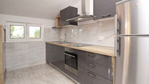 A modern kitchen with a stainless steel refrigerator, a built-in oven, a sink, and a window with a view of greenery.