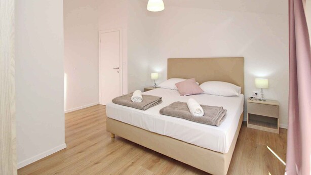 A neatly made bed with two pillows, a bedside table with a lamp, and a door in a simple, clean room.