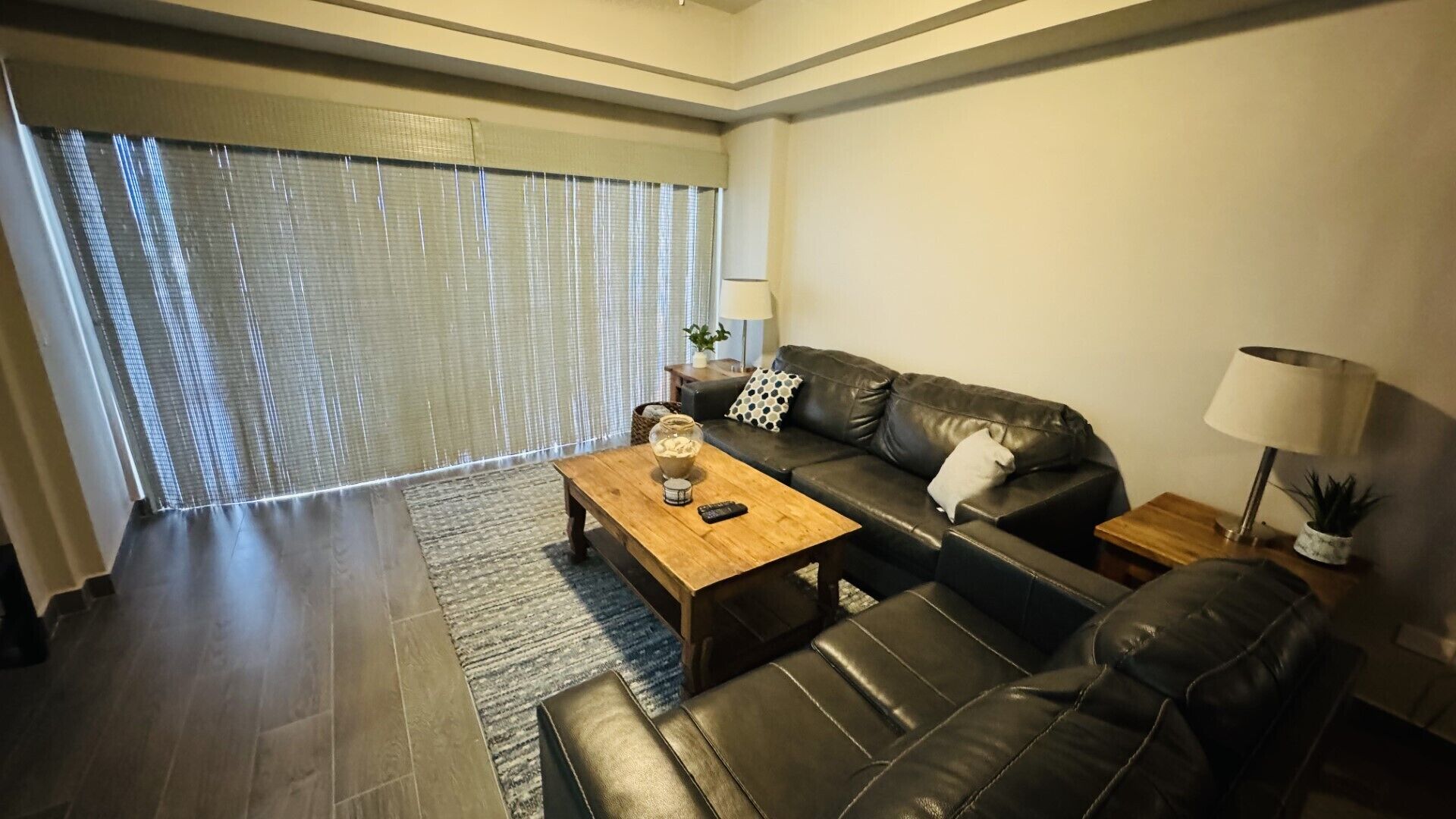 A modern living room with a leather sofa, a wooden coffee table, and a large window with blinds.